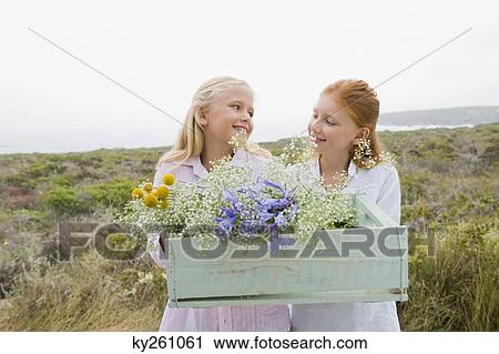 Two girls carrying a box of flowers and smiling View Large Photo Image Stock Image - Two girls carrying a box of flowers and smiling. Fotosearch