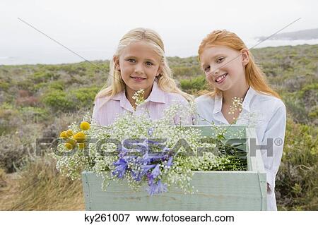Two girls carrying a box of flowers and smiling View Large Photo Image Stock Photo - Two girls carrying a box of flowers and smiling. Fotosearch