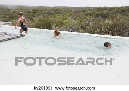 Stock Image - Two girls swimming in an infinity pool with a boy. Fotosearch