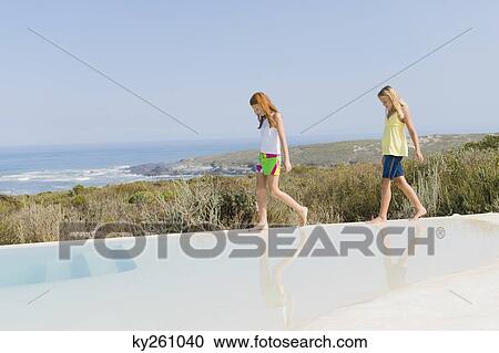 Two girls walking on the ledge of an infinity pool View Large Photo Image Stock Image - Two girls walking on the ledge of an infinity pool. Fotosearch