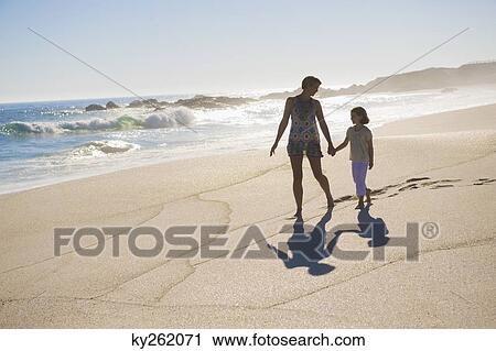 Stock Image - Woman walking on the beach with her daughter. Fotosearch