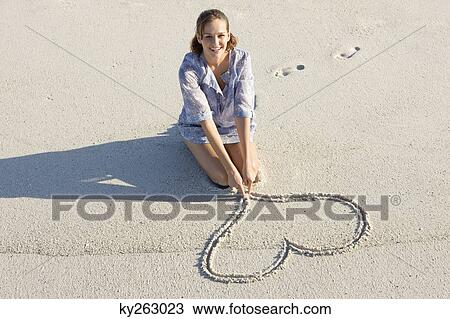 Stock Image - Woman drawing a heart shape on the beach. Fotosearch