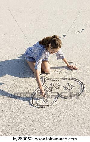 Stock Image - Woman drawing a heart shape on the beach. Fotosearch