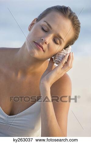 Woman listening to a conch shell View Large Photo Image Stock Photo - Woman listening to a conch shell. Fotosearch