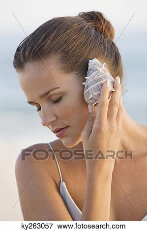 Woman listening to a conch shell View Large Photo Image Stock Photo - Woman listening to a conch shell. Fotosearch