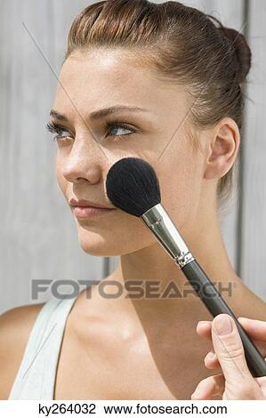 Stock Image - Woman applying make-up on her face. Fotosearch
