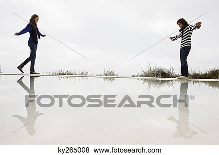 Couple walking on the ledge of a swimming pool View Large Photo Image Stock Photo - Couple walking on the ledge of a swimming pool. Fotosearch