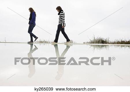 Stock Photo - Couple walking on the ledge of a swimming pool. Fotosearch