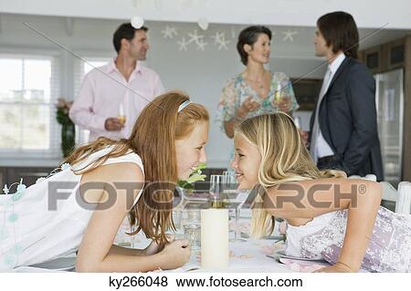 Stock Photo - Girl whispering to her sister across a dining table. Fotosearch