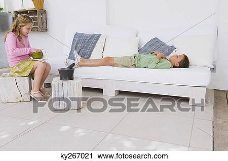 Boy lying on a couch with his sister sitting near him View Large Photo Image Stock Image - Boy lying on a couch with his sister sitting near him. Fotosearch