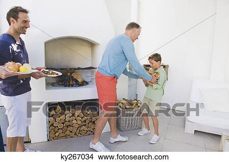 Man cooking kebab in fireplace with his son holding firewood View Large Photo Image Picture - Man cooking kebab in fireplace with his son holding firewood. Fotosearch