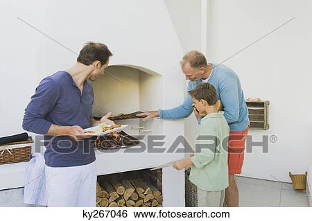 Two Men With A Boy Cooking Kebab At Fireplace Stock Photograph