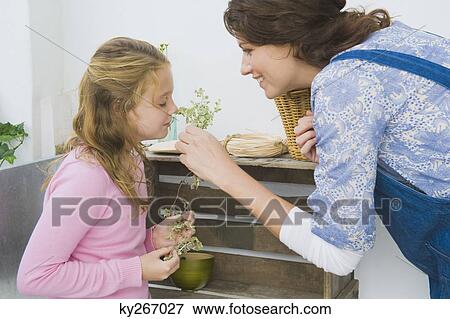 Woman holding plant with her daughter smelling it View Large Photo Image Stock Photo - Woman holding plant with her daughter smelling it. Fotosearch