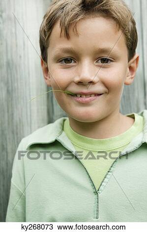 Stock Image - Boy holding a blade of grass in his mouth and smiling. Fotosearch