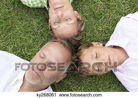 Boy with his parents lying on grass in a park View Large Photo Image Stock Image - Boy with his parents lying on grass in a park. Fotosearch