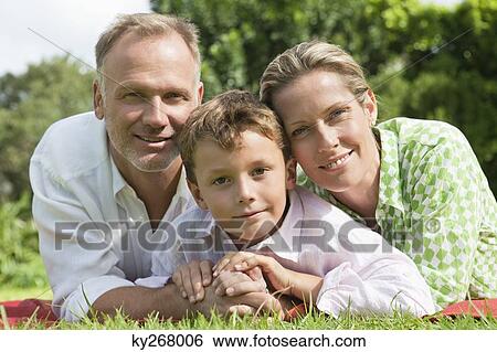 Stock Photograph - Boy with his parents lying on grass in a park. Fotosearch