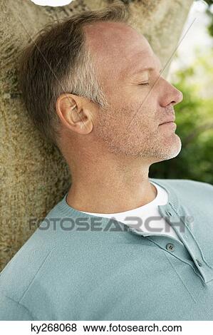Stock Photo - Man leaning against a tree and thinking. Fotosearch