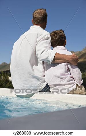 Man sitting with his son on the ledge of a swimming pool View Large Photo Image Stock Photo - Man sitting with his son on the ledge of a swimming pool. Fotosearch