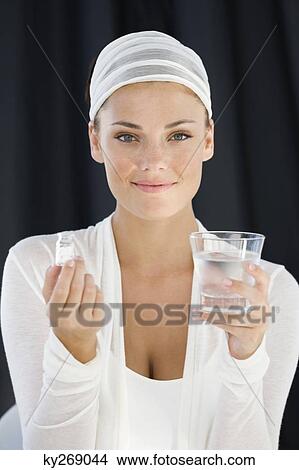 Woman holding a bottle of medicine with a glass of water View Large Photo Image Picture - Woman holding a bottle of medicine with a glass of water. Fotosearch