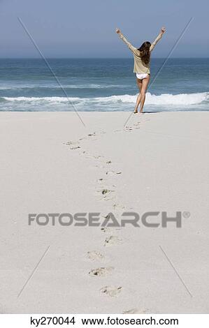 Rear view of a woman standing on the beach with her arms raised View Large Photo Image Picture - Rear view of a woman standing on the beach with her arms raised. Fotosearch