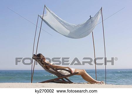 Stock Image - Woman resting in a deck chair under a canopy. Fotosearch