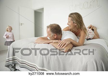 Couple lying on the bed and looking at their daughter View Large Photo Image Stock Photo - Couple lying on the bed and looking at their daughter. Fotosearch
