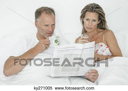 Couple reading newspaper on the bed View Large Photo Image Stock Photography - Couple reading newspaper on the bed. Fotosearch