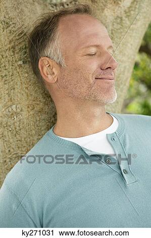 Stock Image - Man leaning against a tree trunk. Fotosearch