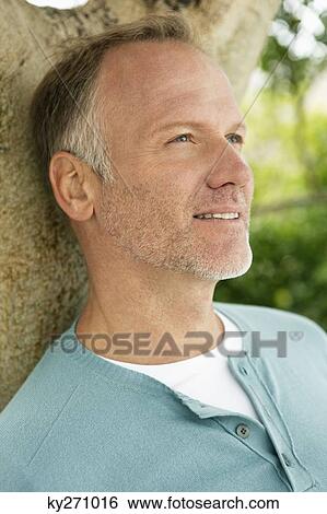 Stock Photograph - Man leaning against a tree trunk. Fotosearch