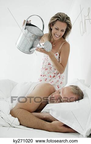 Woman pouring water with a watering can on a man sleeping on the bed View Large Photo Image Stock Image - Woman pouring water with a watering can on a man sleeping on the bed. Fotosearch