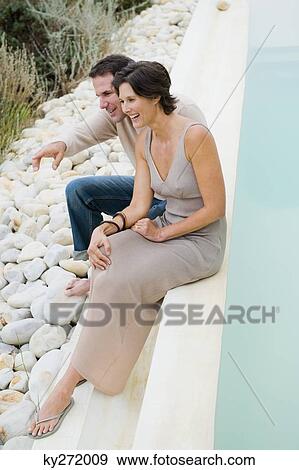 Stock Photo - Couple sitting at the poolside and admiring the view. Fotosearch
