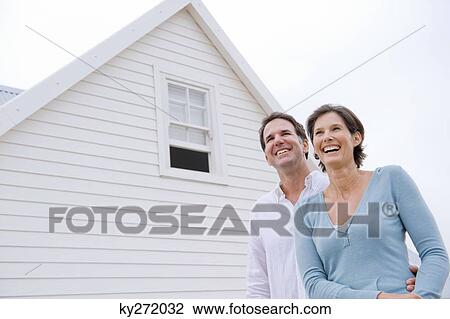 Couple smiling with a house in the background View Large Photo Image Stock Image - Couple smiling with a house in the background. Fotosearch