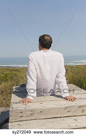 Rear view of a man sitting on a boardwalk View Large Photo Image Stock Photo - Rear view of a man sitting on a boardwalk. Fotosearch