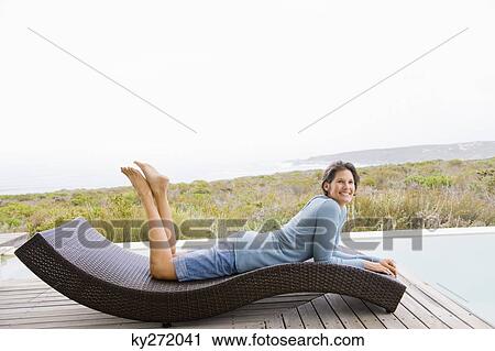 Stock Image - Woman lying on a chaise longue at the poolside. Fotosearch