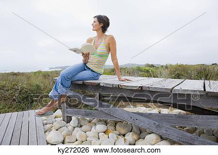 Stock Photograph - Woman sitting on a boardwalk and reading a book. Fotosearch