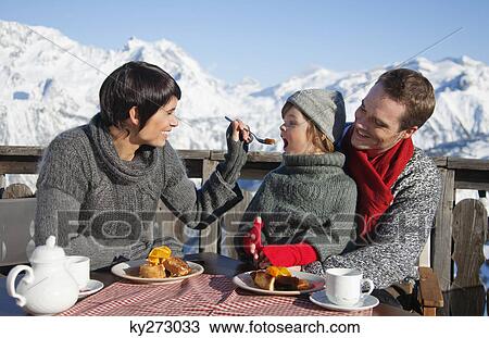 Stock Image - Couple and daughter eating on balcony at ski resort. Fotosearch