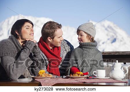 Stock Photo - Couple and daughter eating on balcony at ski resort. Fotosearch