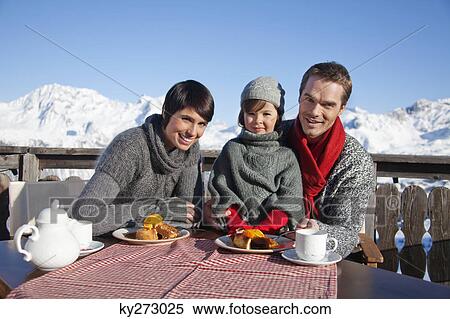 Stock Photography - Couple and daughter eating on balcony at ski resort. Fotosearch