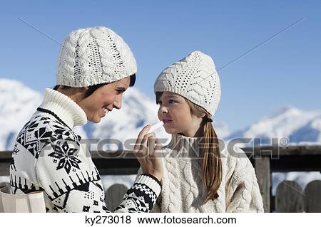 Stock Photo - Mother applying lip balm to her daughter. Fotosearch