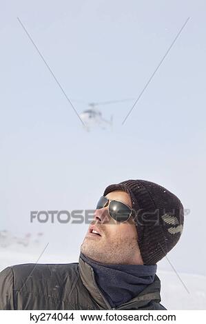 Portrait of young man in winter clothes looking up, helicopter in background View Large Photo Image Picture - Portrait of young man in winter clothes looking up, helicopter in background. Fotosearch