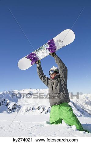 Young man holding his snowboard above his head View Large Photo Image Stock Image - Young man holding his snowboard above his head. Fotosearch