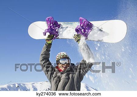 Young man holding his snowboard above his head View Large Photo Image Stock Photograph - Young man holding his snowboard above his head. Fotosearch