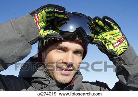 Young man looking at camera, removing his ski goggles View Large Photo Image Stock Photo - Young man looking at camera, removing his ski goggles. Fotosearch