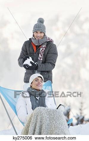 Stock Photograph - Young man about to throw snowball at woman resting. Fotosearch