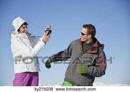 Young woman in ski wear taking a photo of her boyfriend View Large Photo Image Stock Photo - Young woman in ski wear taking a photo of her boyfriend. Fotosearch