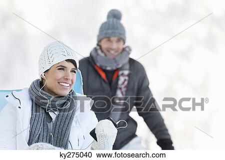 Young woman in winter clothes listening to music, man in background View Large Photo Image Stock Image - Young woman in winter clothes listening to music, man in background. Fotosearch
