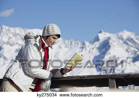 Young woman reading a book, enjoying winter sun, mountains in background View Large Photo Image Picture - Young woman reading a book, enjoying winter sun, mountains in background. Fotosearch