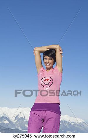 Young woman with arms raised, smiling at camera, mountains in background View Large Photo Image Stock Photography - Young woman with arms raised, smiling at camera, mountains in background. Fotosearch