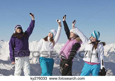 Stock Image - Four teenage girls in ski clothes, with their mobile phones in air. Fotosearch