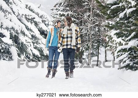 Stock Image - Young couple looking at each other, walking in snow. Fotosearch